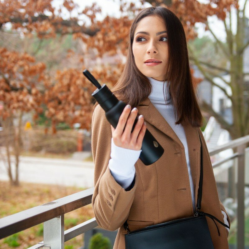 Kobieta z czarną butelką, brązowym płaszczem.