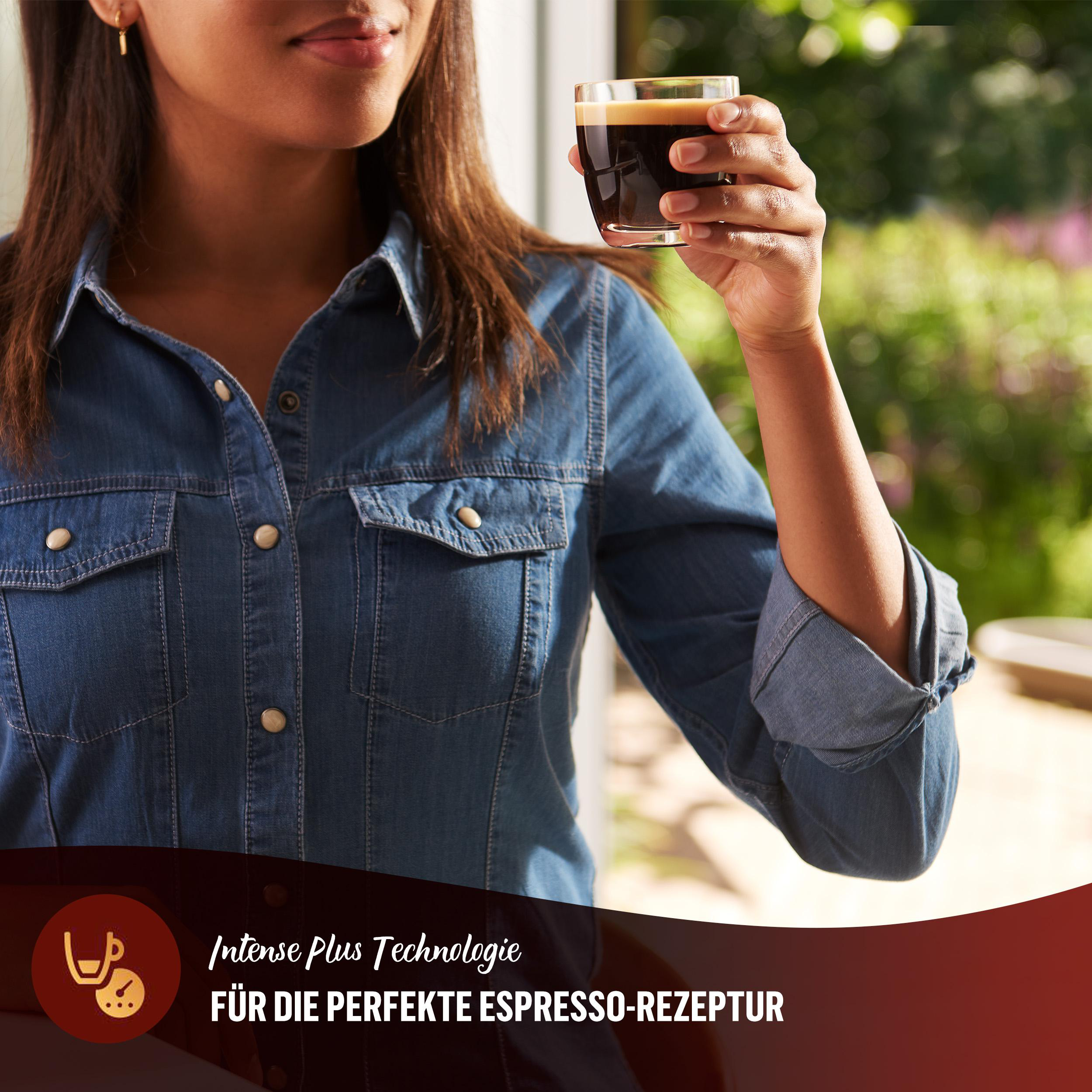 Frau hält ein Kaffeeglas. Sie trägt ein Jeanshemd. Im Hintergrund sieht man ein Fenster und ein Logo zum perfekten Espresso.