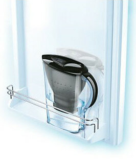 Czarny i przezroczysty dzbanek z filtrem wody na białej półce lodówki.