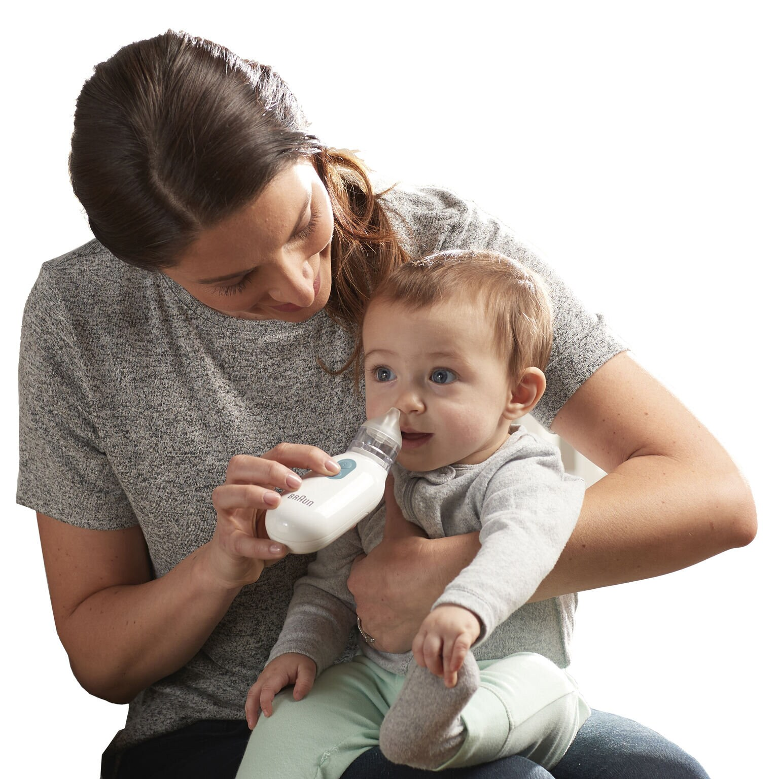 Kobieta trzyma dziecko, używając aspiratora do nosa. Dziecko patrzy na urządzenie z zainteresowaniem.