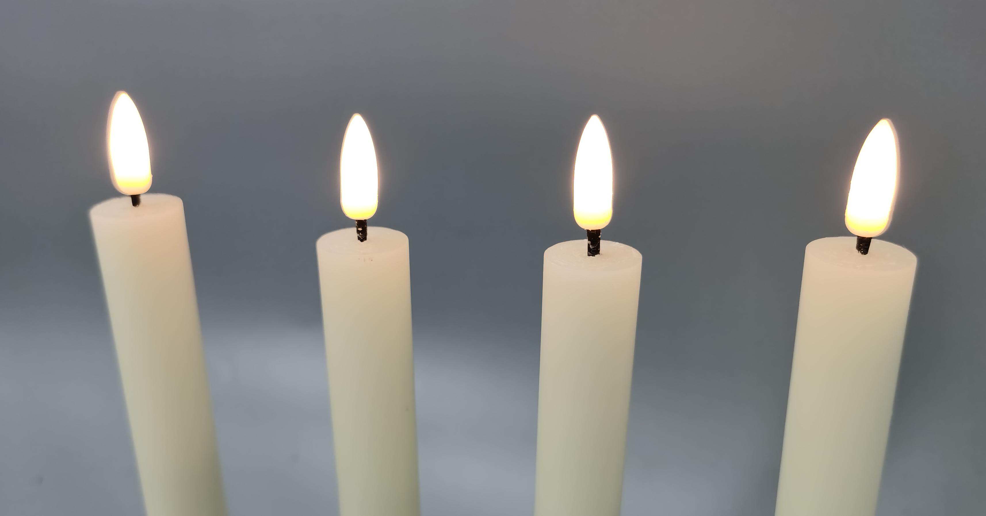 Vier brennende weiße Kerzen vor grauem Hintergrund. Jede Kerze hat eine helle, flackernde Flamme.