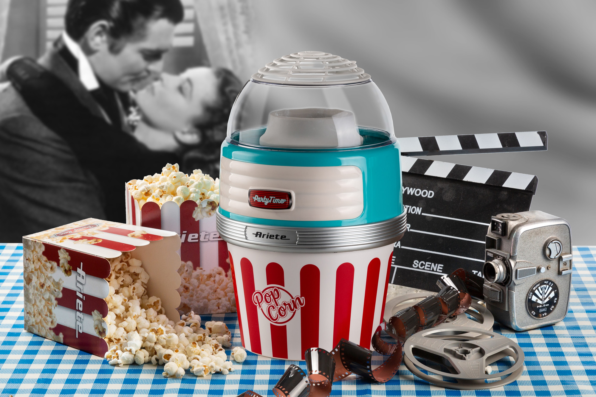 Egy pattogatott kukorica készítő, pattogatott kukorica dobozok, filmszalag és egy filmes csapó az kockás asztalon. Csókolózós jelenet.