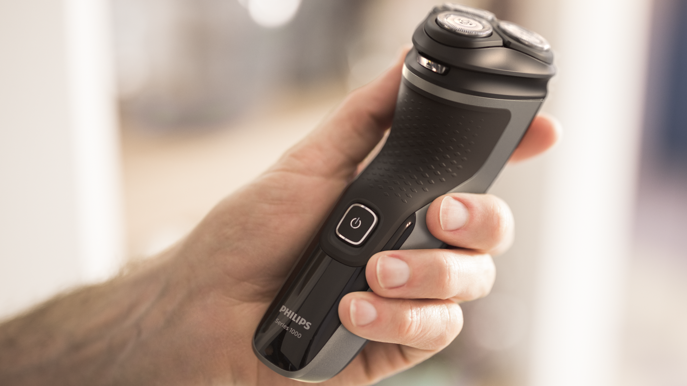 Ręka trzymająca czarno-szarą golarkę elektryczną Philips Series 1000.