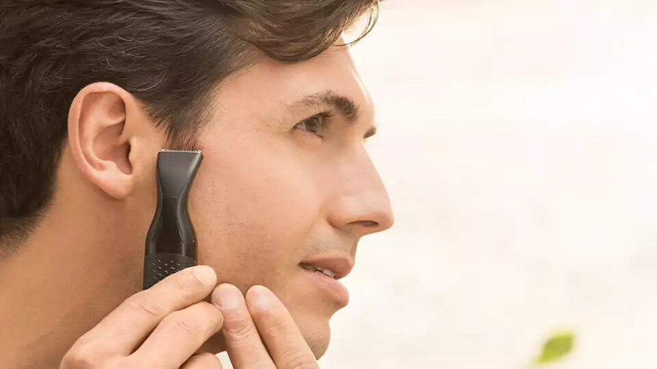 Mężczyzna używający czarnej trymer na twarzy, trymer jest blisko jego policzka.