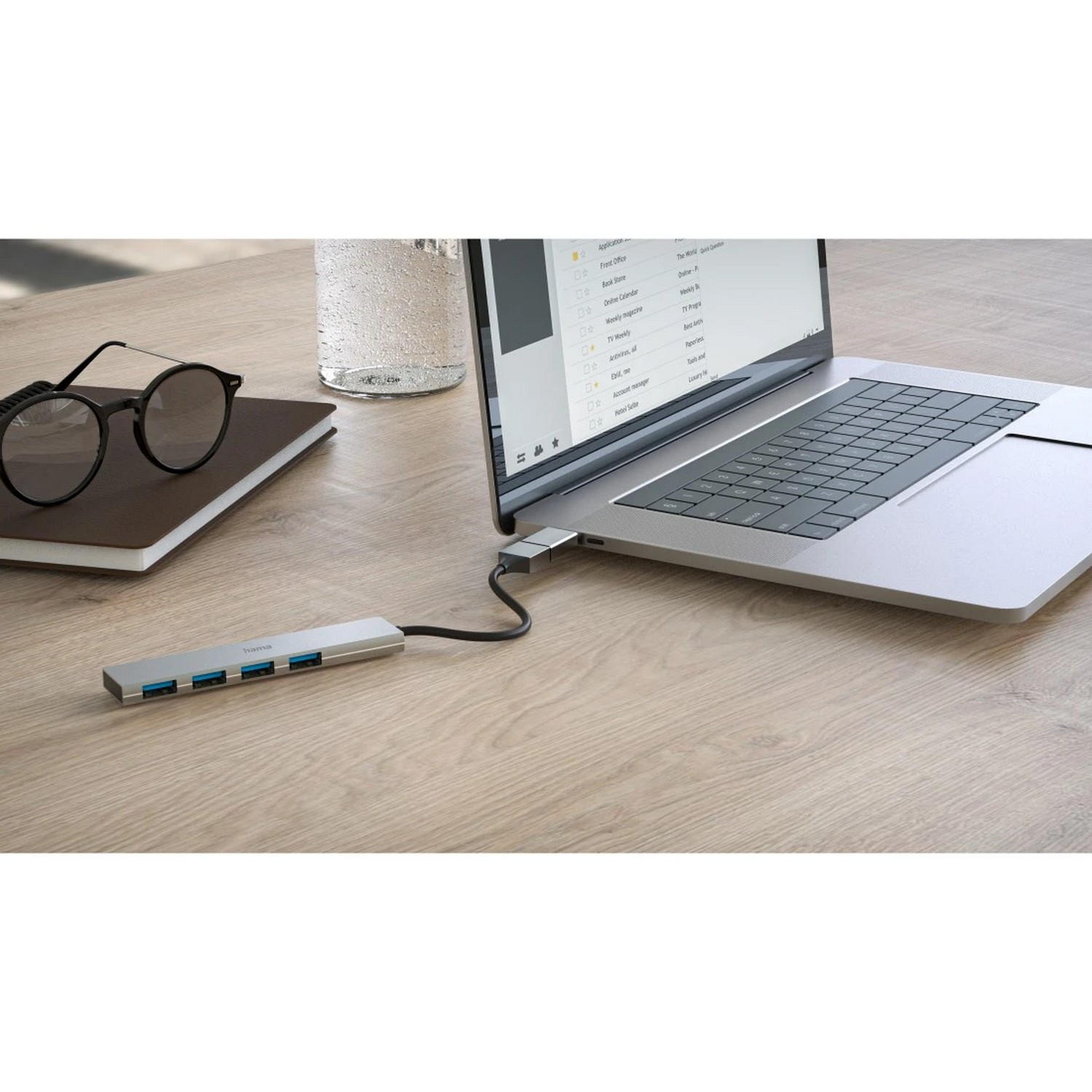 Ordinateur portable avec un hub USB, des lunettes et un verre d'eau sur une table en bois.