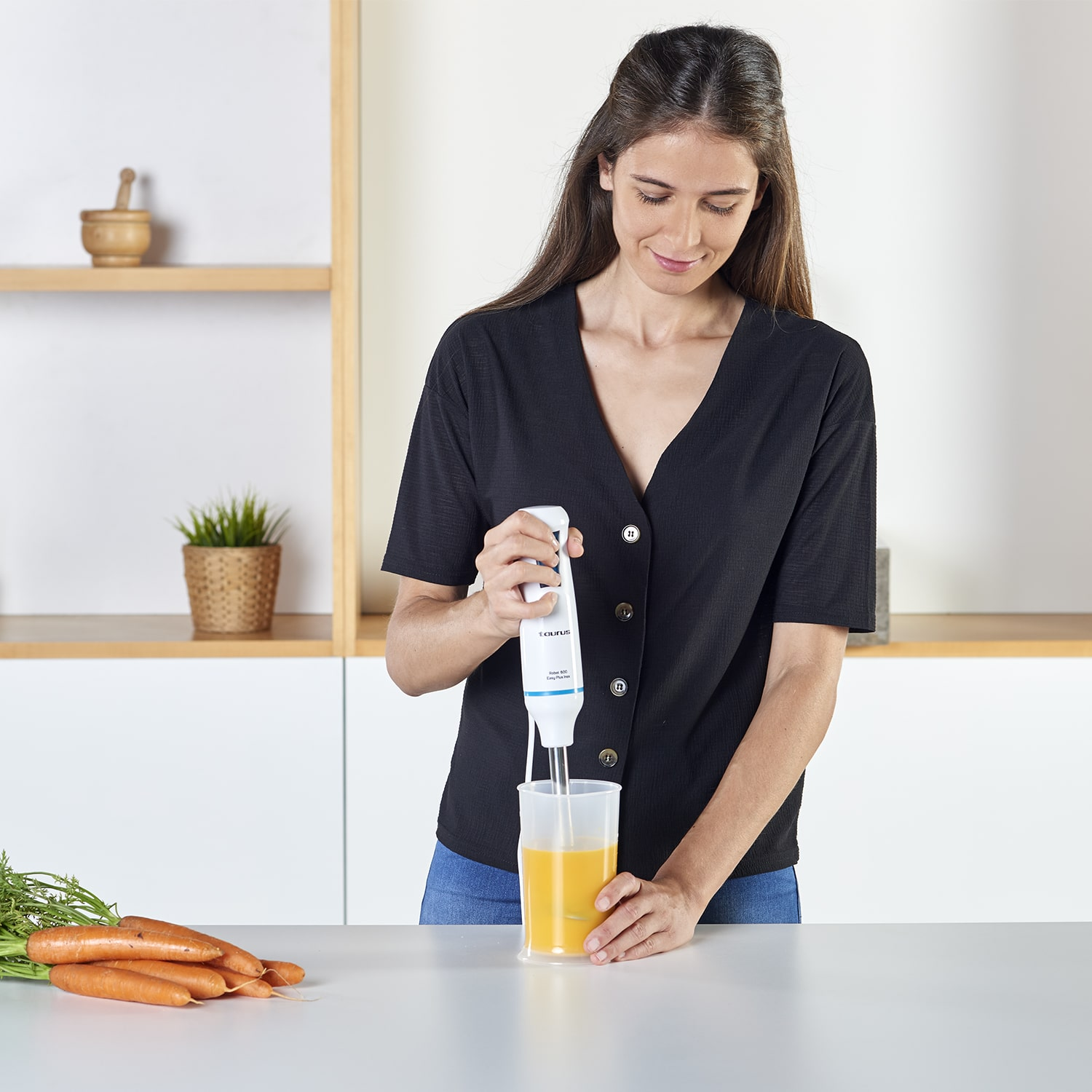 Mujer usando una batidora de mano blanca. Hay zanahorias en la mesa.