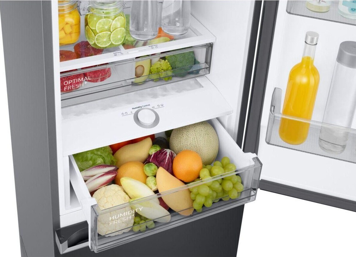 Otwarta lodówka z owocami i warzywami w szufladach. Widoczna również butelka soku.