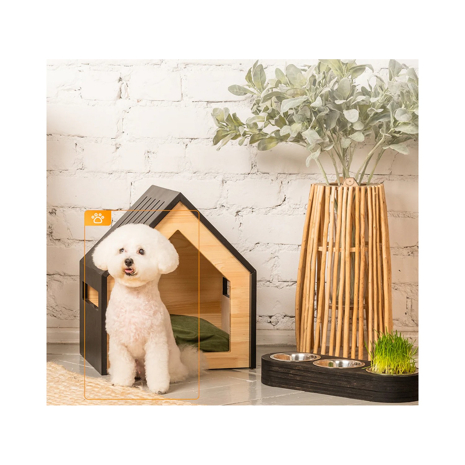 White dog sitting in a wooden dog house, with food bowls and plant. The background is a brick wall.