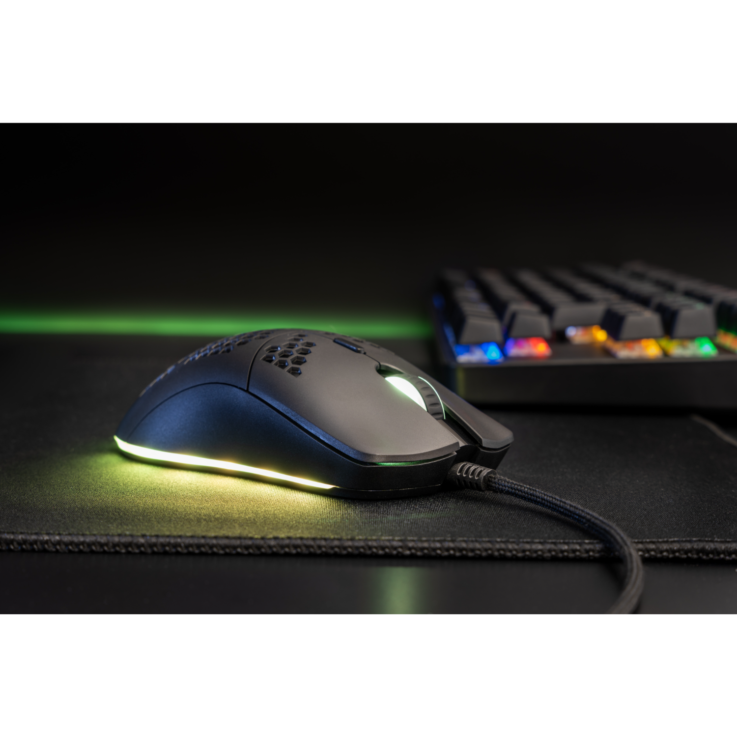 Black gaming mouse with a honeycomb design and illuminated edges. Keyboard is in the background.