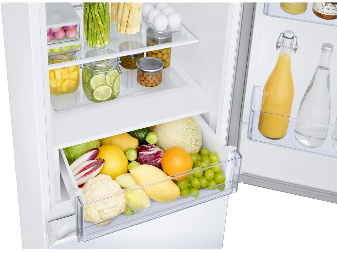 Intérieur de réfrigérateur avec fruits, légumes et boissons. Un tiroir rempli de produits est visible.