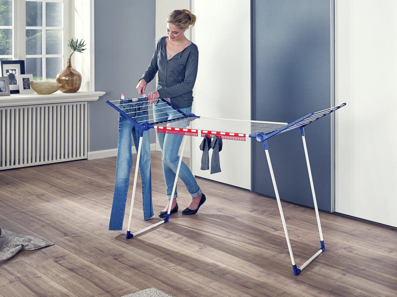 Eine Frau hängt Jeans auf einen Wäscheständer in einem Raum mit Holzboden.