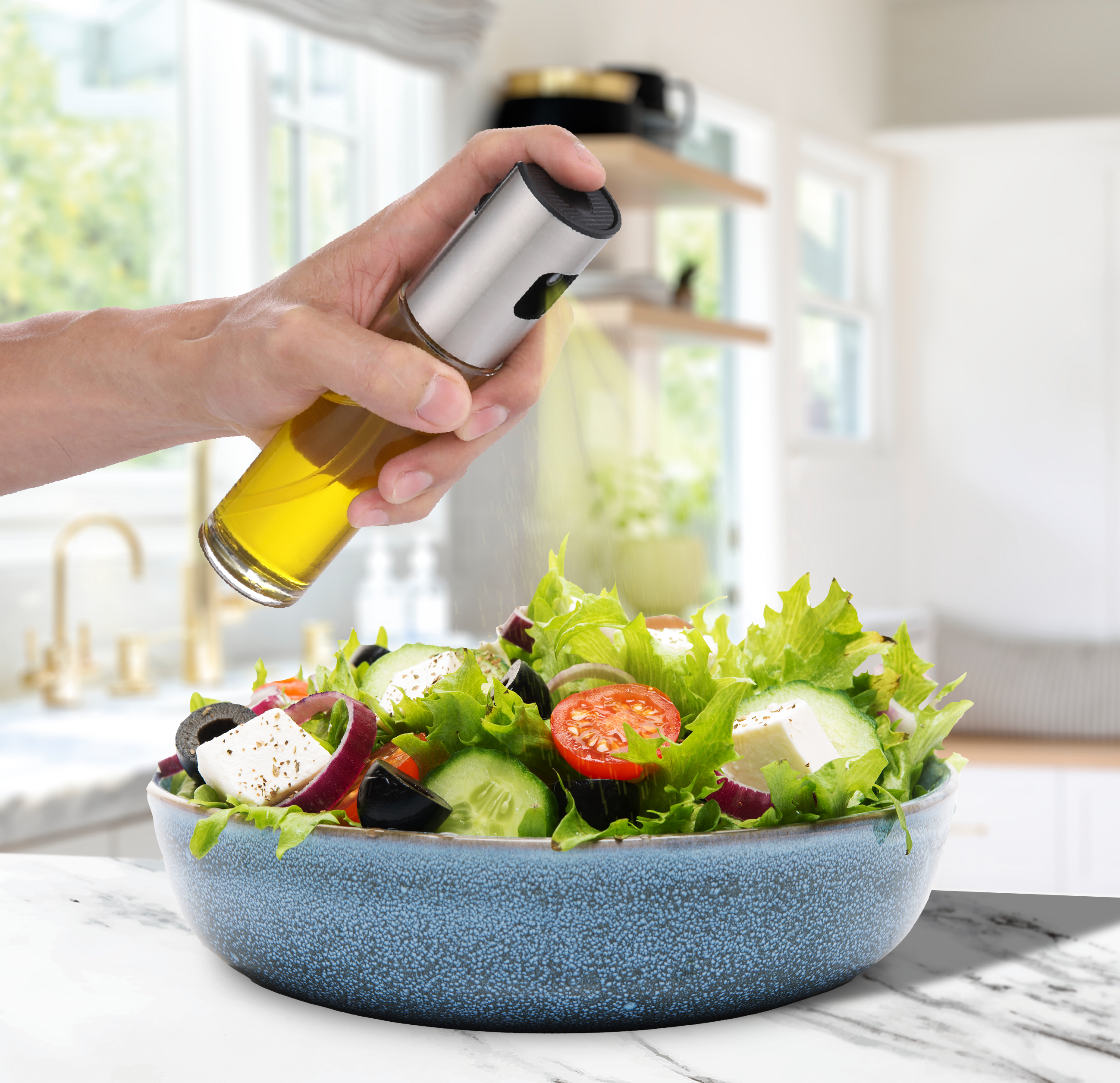 Mano rociando aceite sobre ensalada en cuenco azul. Fondo de cocina.