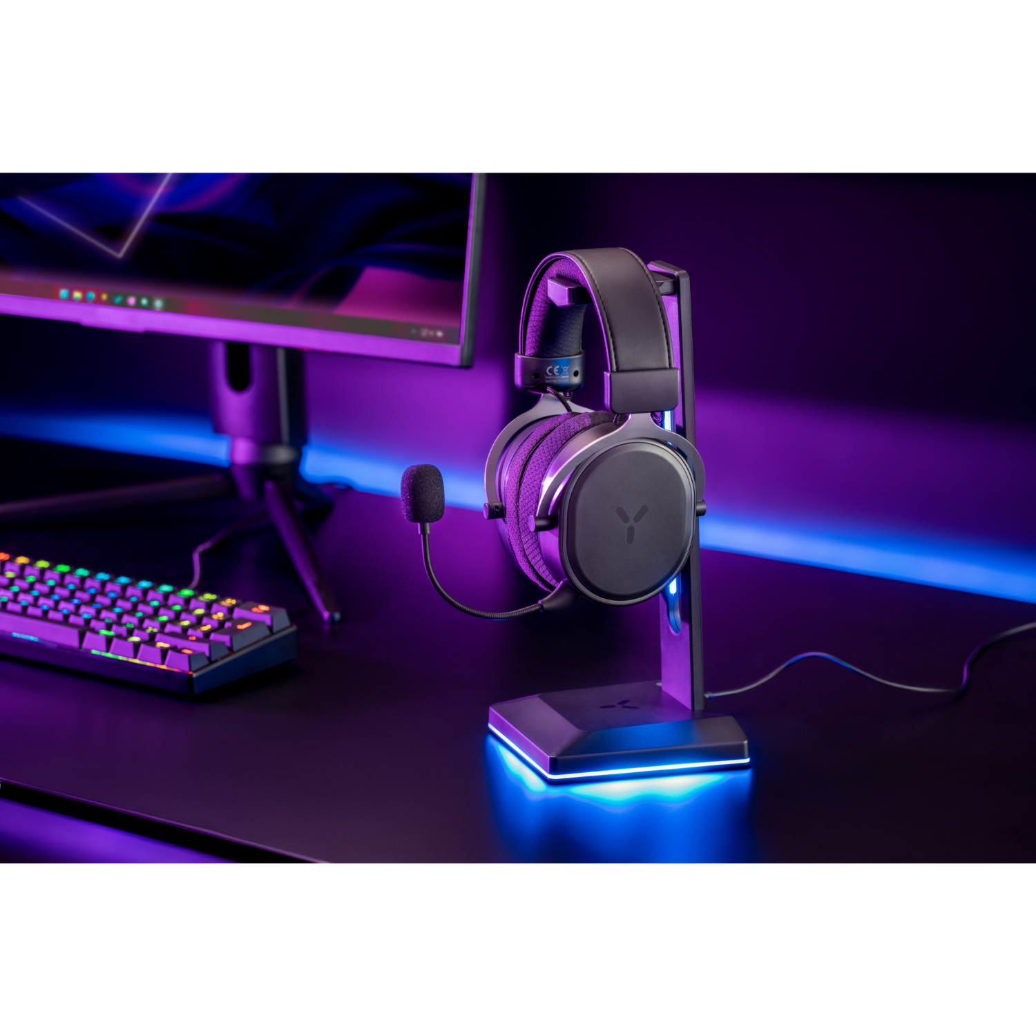 Zwarte gaming headset op standaard, zwart bureau, blauwe en paarse verlichting. Toetsenbord zichtbaar.