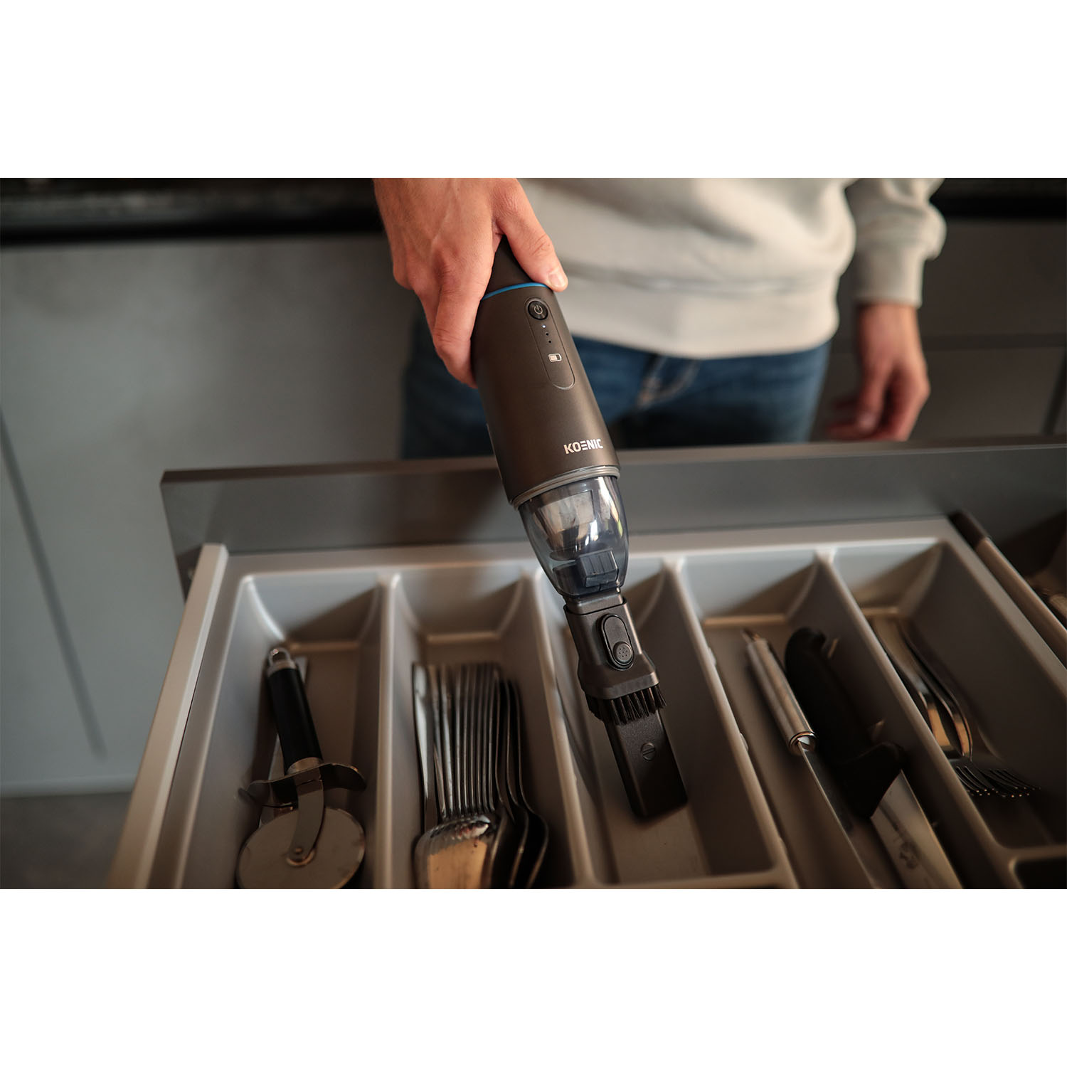 Una mano che ripone un aspirapolvere nero in un cassetto della cucina.