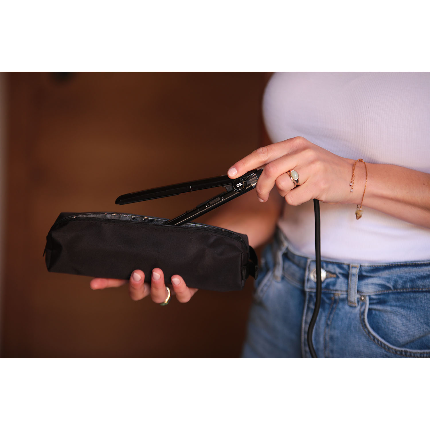 Una persona tiene in mano una piastra per capelli nera, mettendola in un astuccio nero.