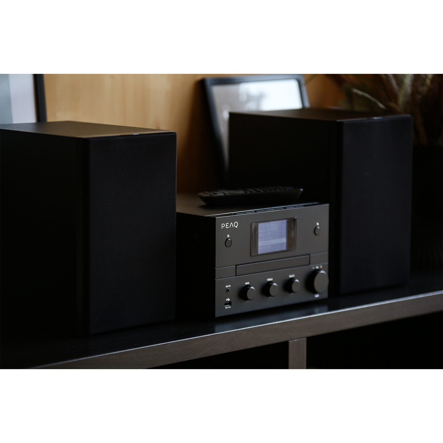 Impianto stereo nero su una mensola, con altoparlanti e un telecomando. Lo sfondo è neutro.