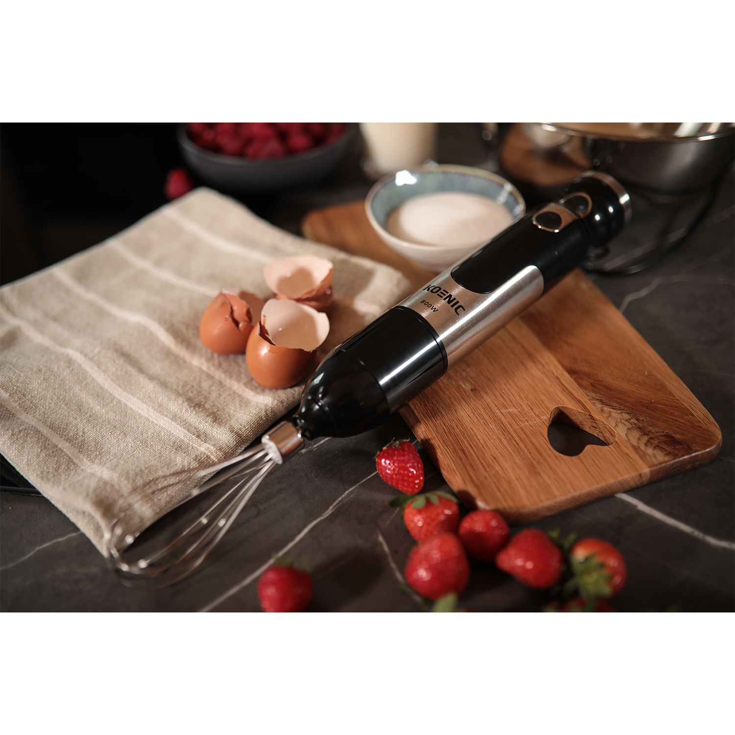 Un frullatore a immersione Koenic, fragole, uova e un tagliere di legno.