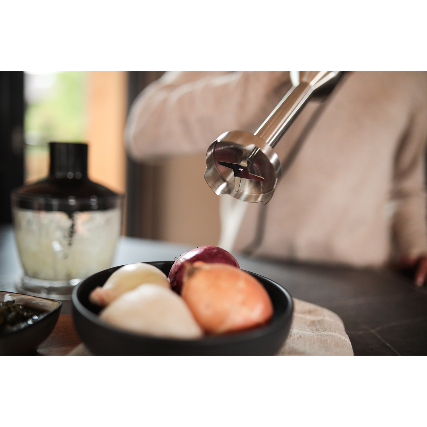 Frullatore a immersione con lama rivolta verso una ciotola di cipolle e altri ingredienti.