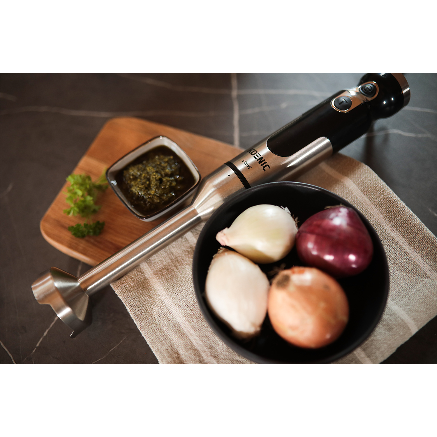 Un frullatore a immersione con ingredienti: cipolle, erbe e pesto.