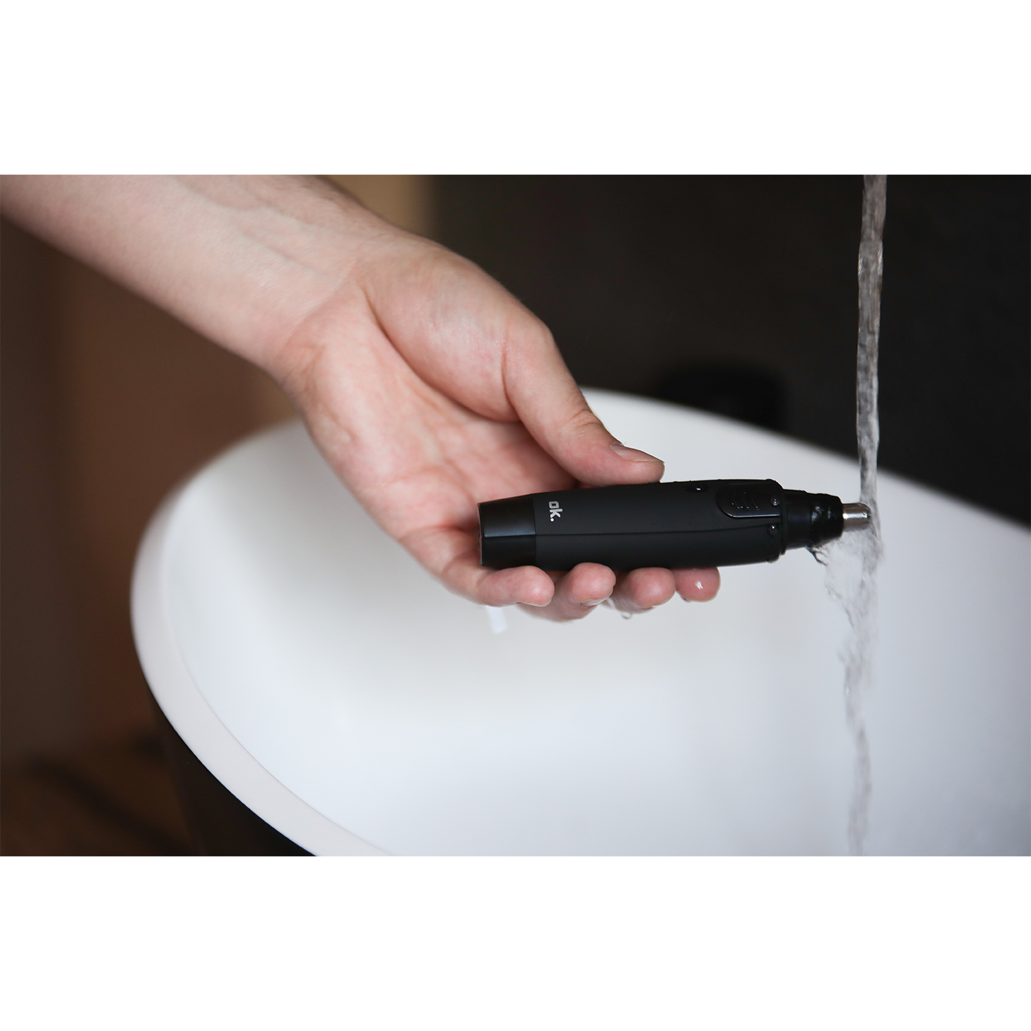Un rifinitore per peli del naso nero viene risciacquato sotto l'acqua corrente in un lavandino bianco.