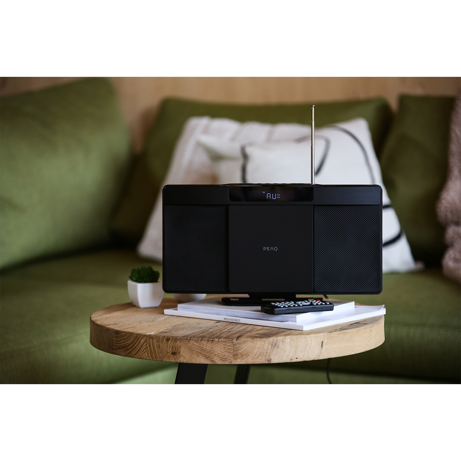 Stereo nero su un tavolo di legno, libro e telecomando. Divano verde sullo sfondo.