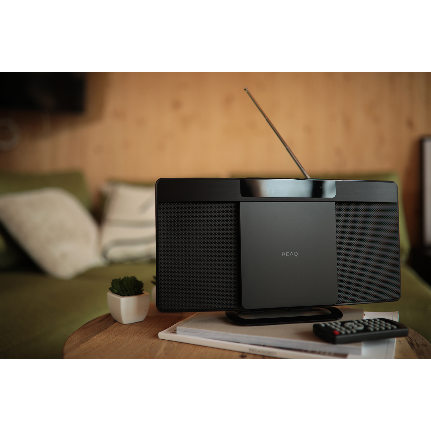 Dispositivo audio nero su un tavolo di legno. Una piccola pianta, libri e un telecomando sono anch'essi sul tavolo.