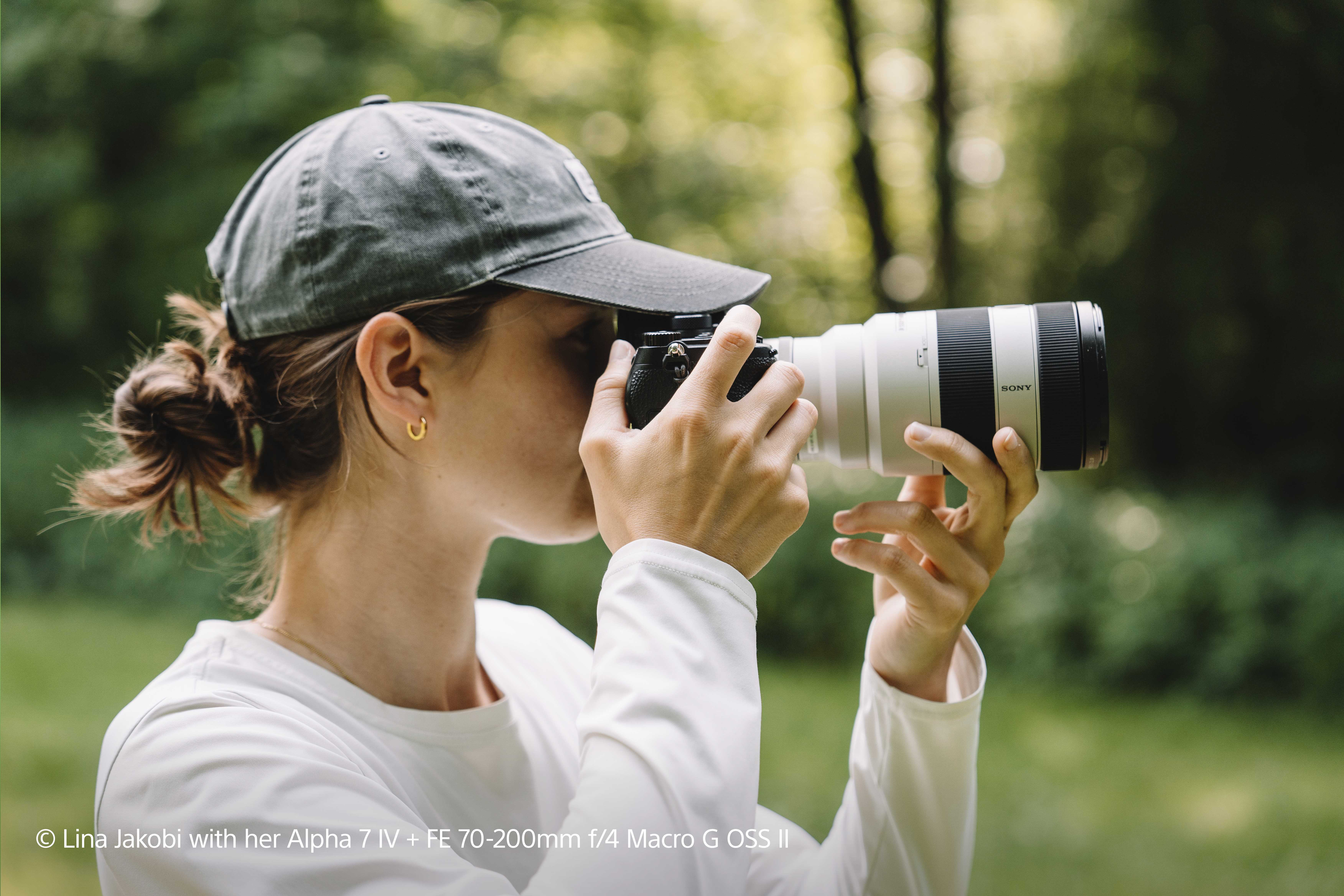 Eine Frau, die eine Kamera mit einem langen Objektiv hält und in einem Park fotografiert.