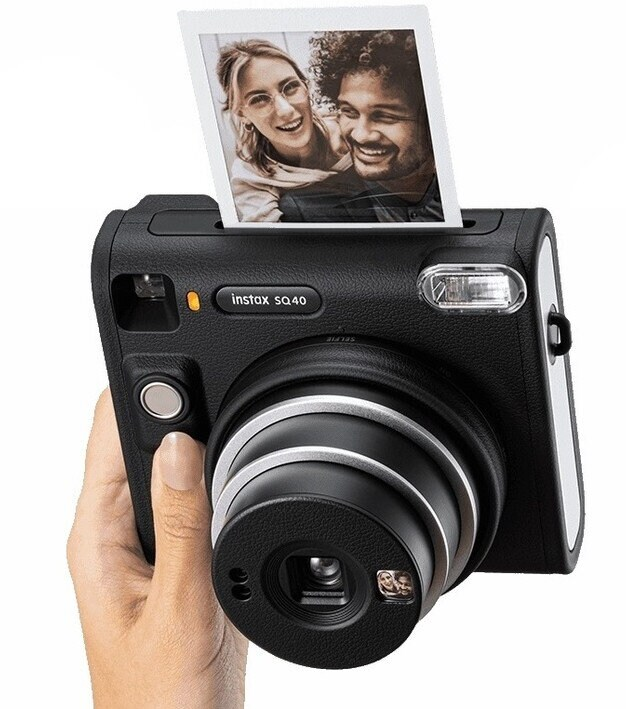 Czarny aparat Instax w dłoni, zdjęcie z ludźmi wysuwa się.