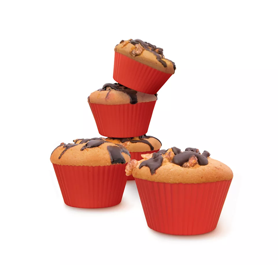 Cztery babeczki w czerwonych papierowych kubeczkach, posypane orzechami i czekoladą. Jedna jest lekko przechylona.
