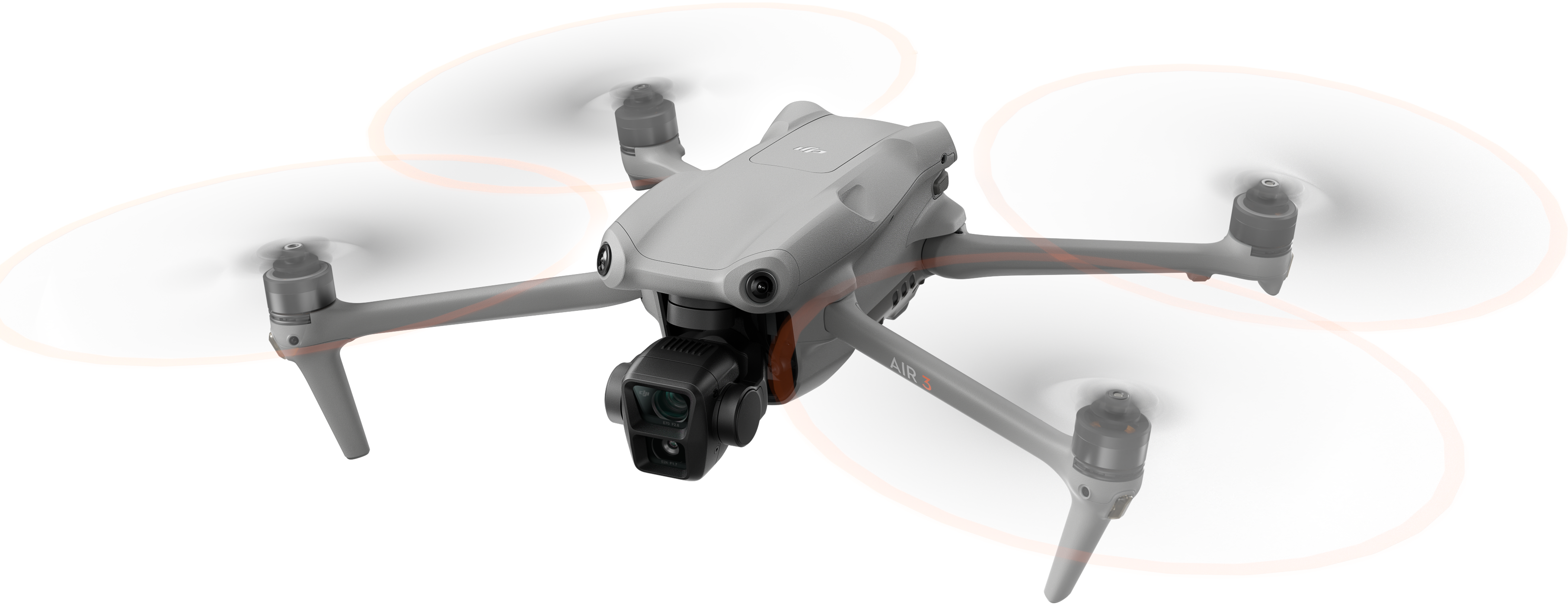 Un drone grigio con quattro eliche in aria. Le pale girano. Accenti arancioni.