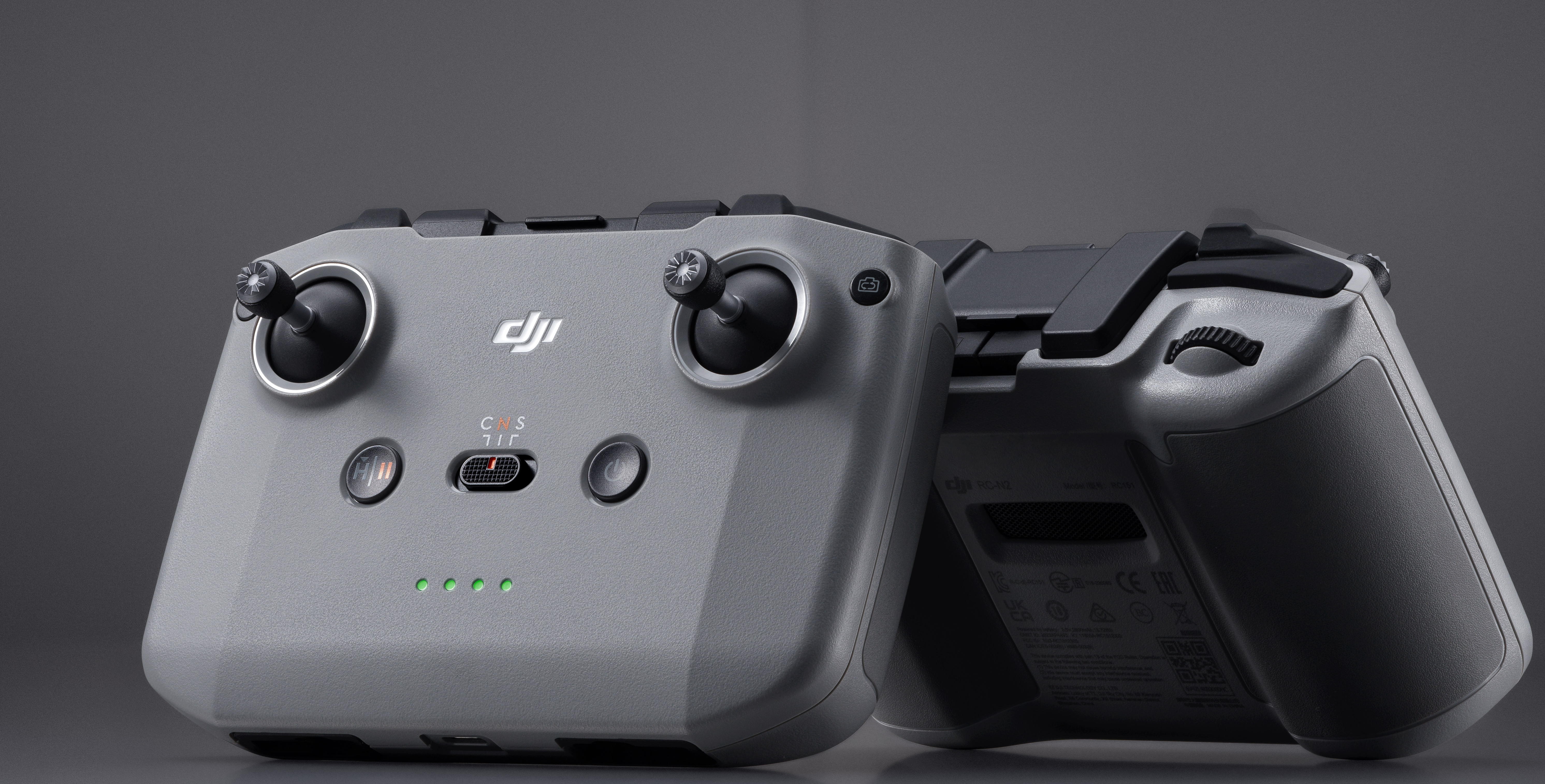 Due controller per droni grigi. Hanno joystick e pulsanti. I controller sono su una superficie grigia.