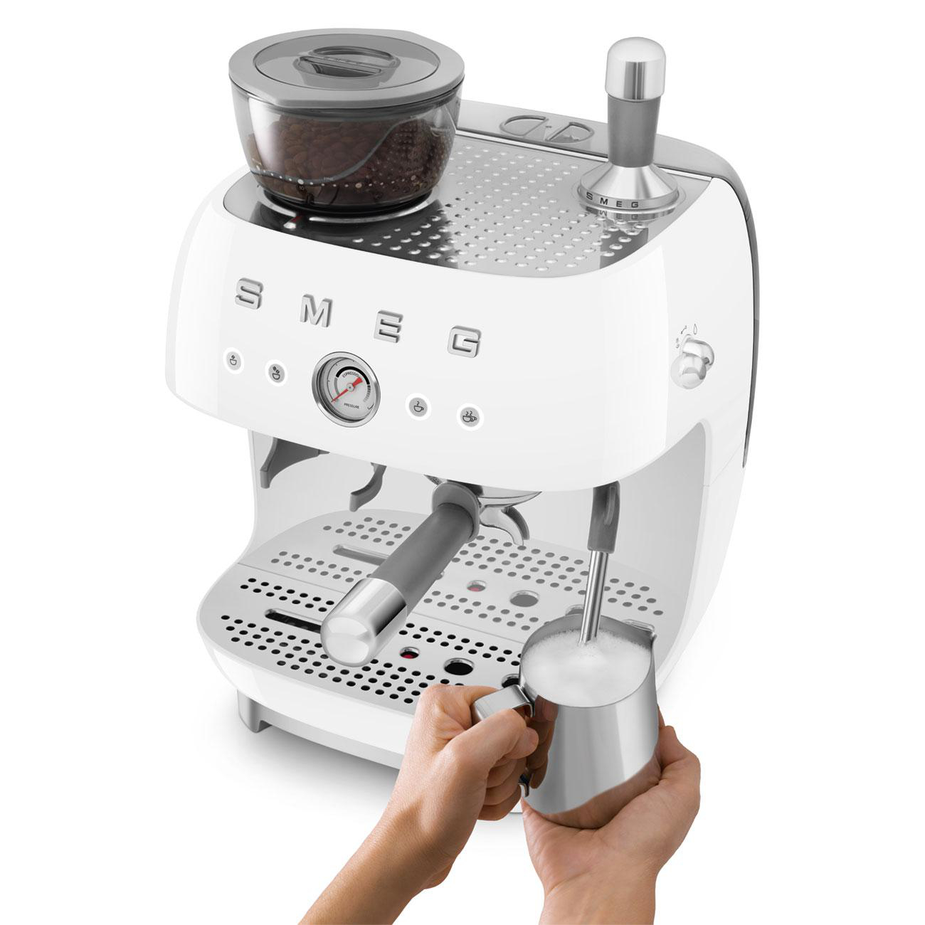 Eine weiße SMEG Espressomaschine, eine Hand schäumt Milch in einen silbernen Krug.