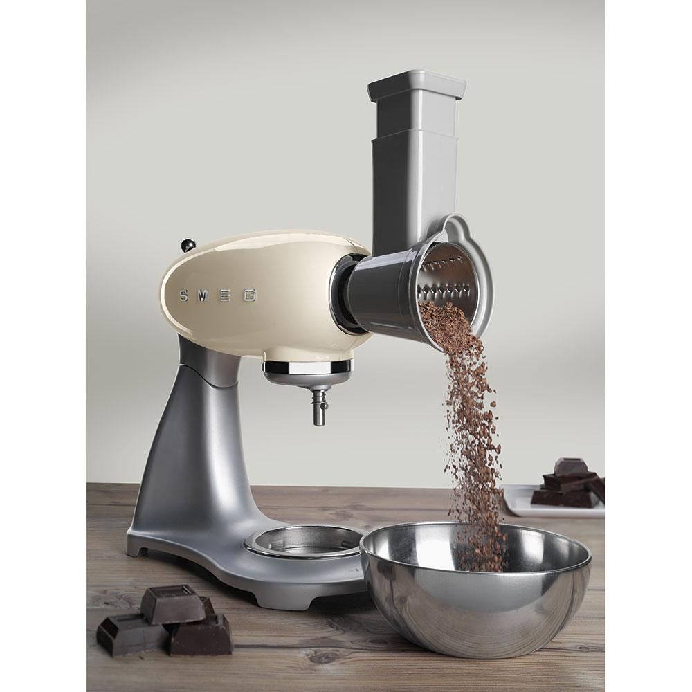 Ein cremefarbener SMEG-Foodprozessor wird gezeigt. Schokolade wird in eine Edelstahlschüssel gerieben.