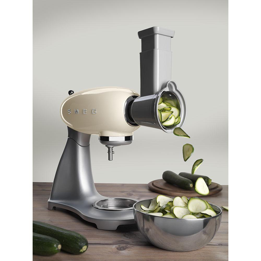 Ein cremefarbener Foodprozessor, der Zucchini in eine Schüssel raspelt. Zucchini und Schüssel sind sichtbar.