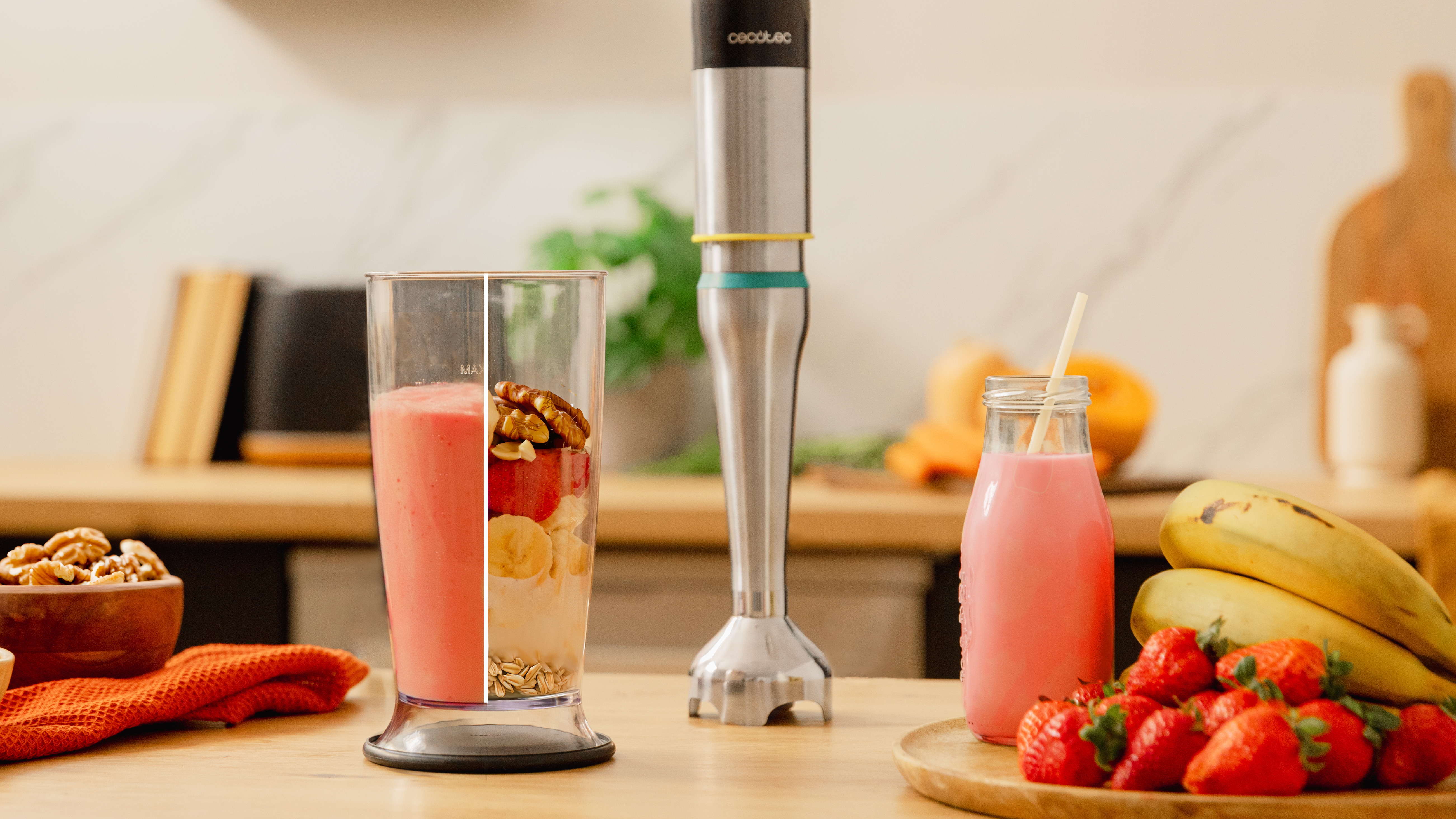 Licuadora con ingredientes en un vaso, batido rosa, frutas y una batidora de mano.