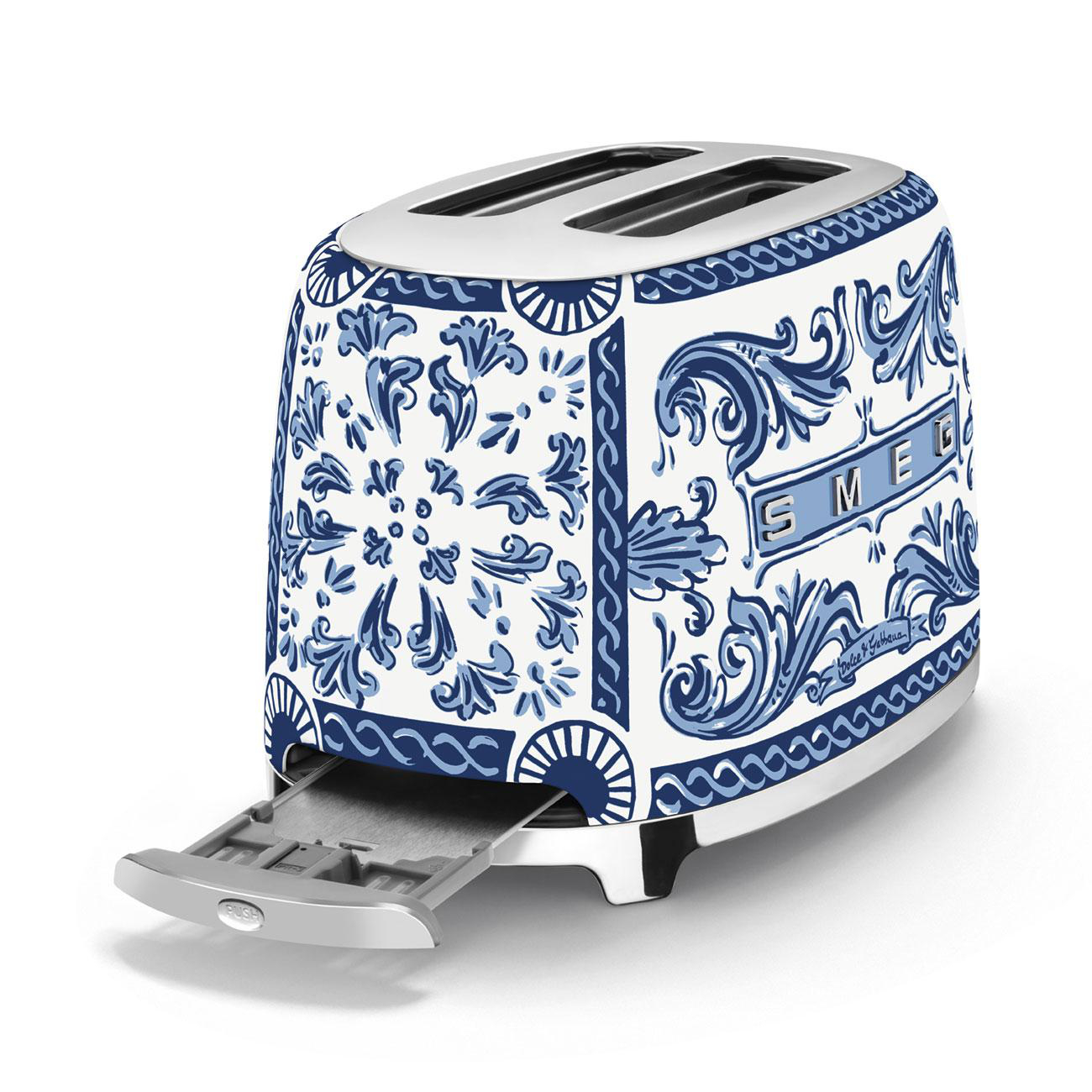 Weißer und blauer floraler Smeg-Toaster. Die Krümelschublade ist geöffnet. Er steht auf einer weißen Oberfläche.