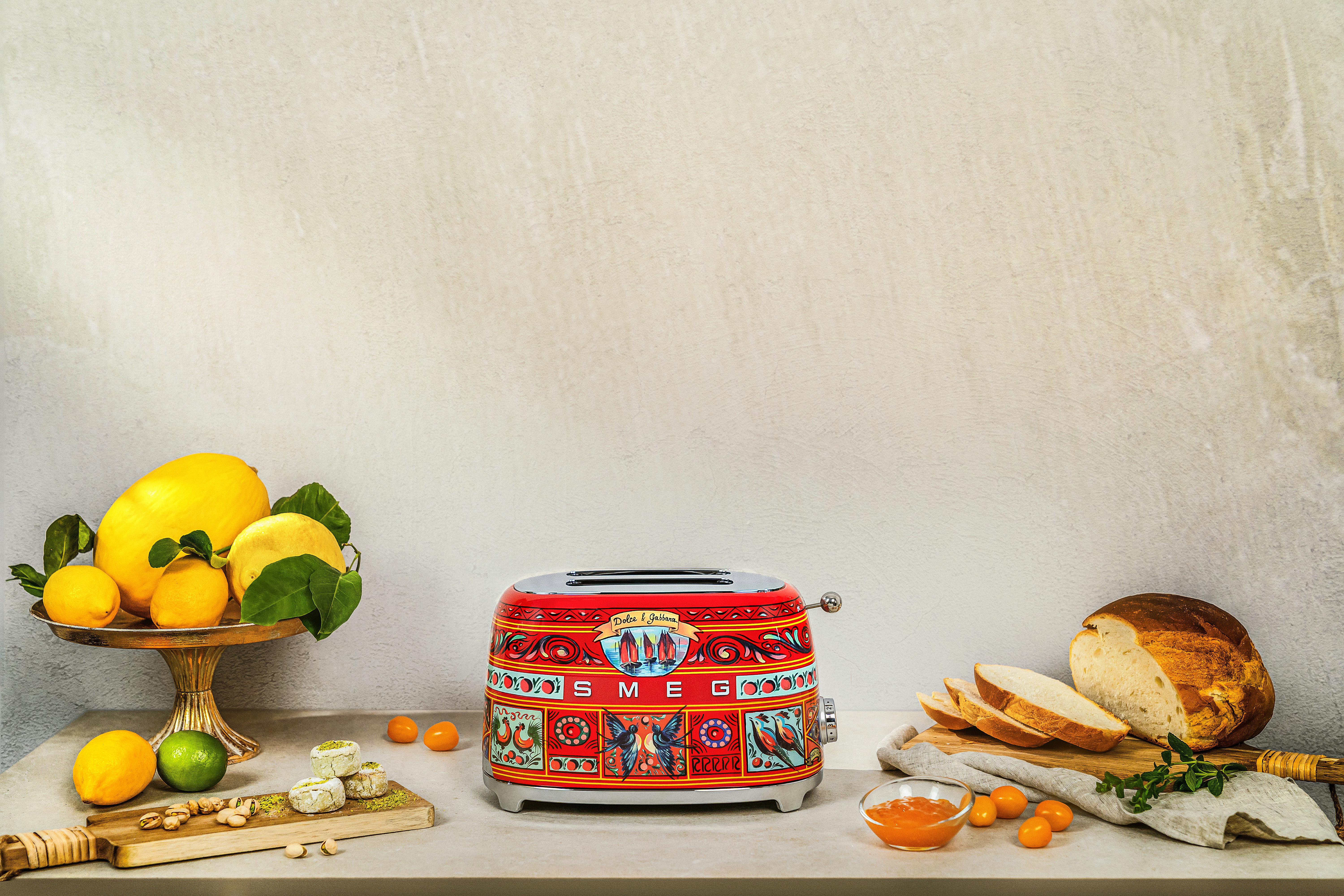 Ein roter und dekorativer Toaster mit Zitronen, Brot und einem Schneidebrett im Vordergrund.