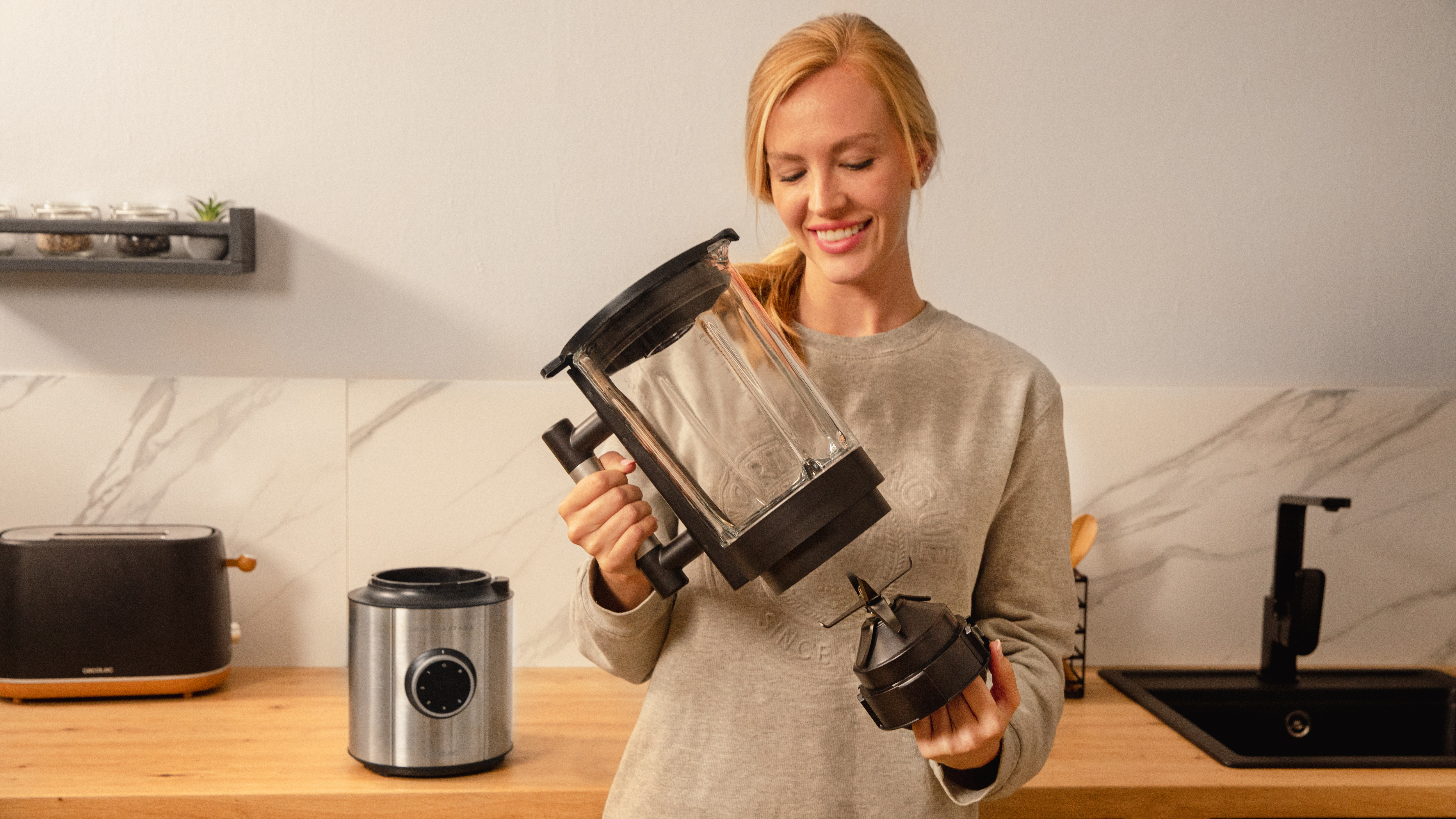 Mujer sosteniendo partes de una licuadora. Base de acero inoxidable y recipiente de vidrio.