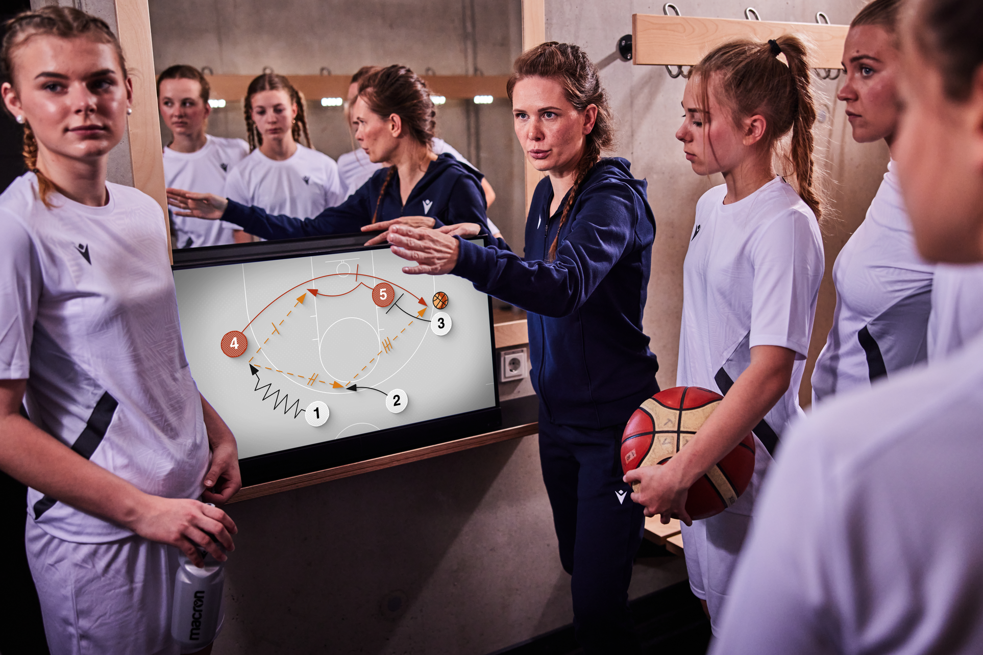 Ein Basketballtrainer zeigt einem Team mit einem Bildschirm ein Spiel. Mädchen sind dabei.
