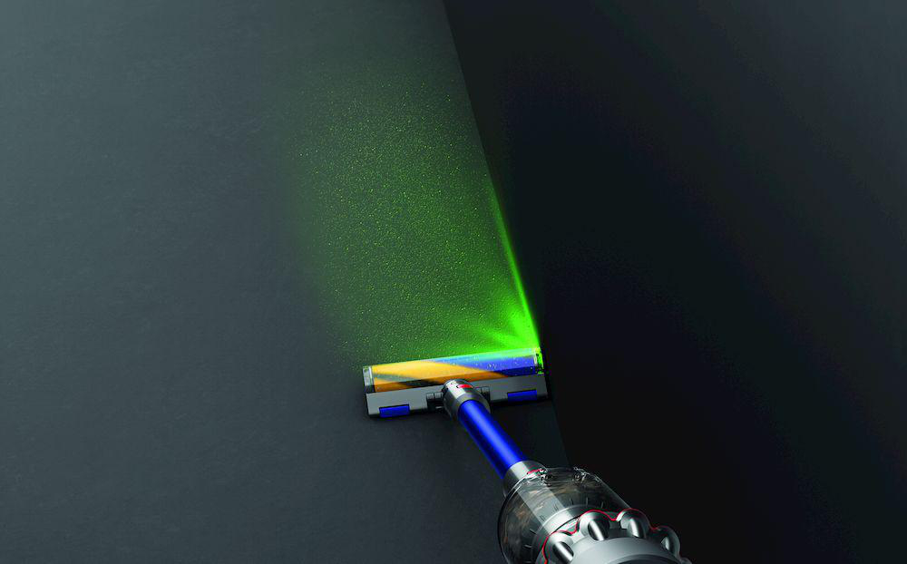 Staubsaugerkopf mit grünem Laserlicht auf dunkler Oberfläche.