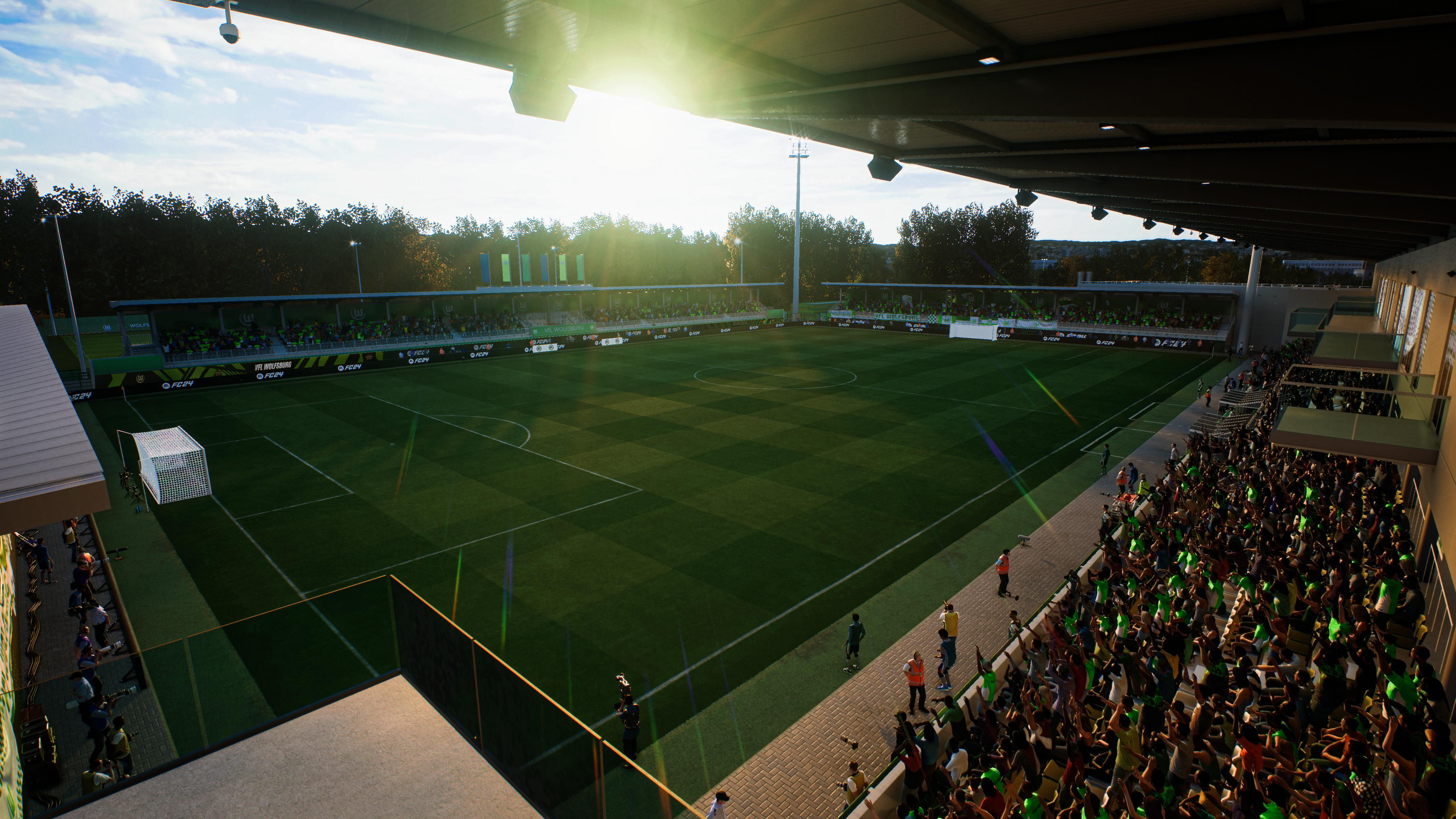 Ein Fußballfeld mit grünem Gras und ein Stadion mit Fans. Der Himmel ist blau mit Wolken.