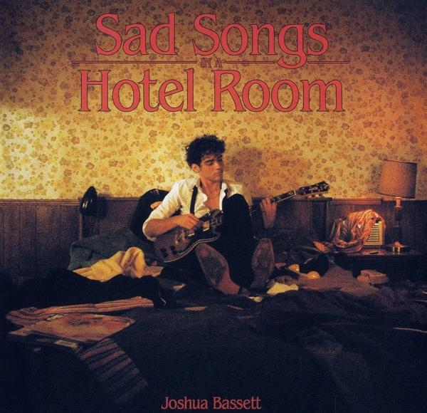 Albumcover mit Mann, der Gitarre in Hotelzimmer spielt.