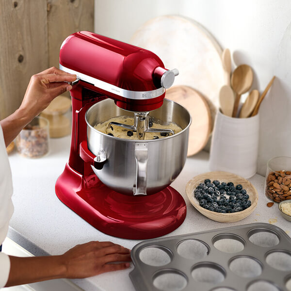 Egy piros állványos mixer, amely hozzávalókat kever áfonyával egy tálban.