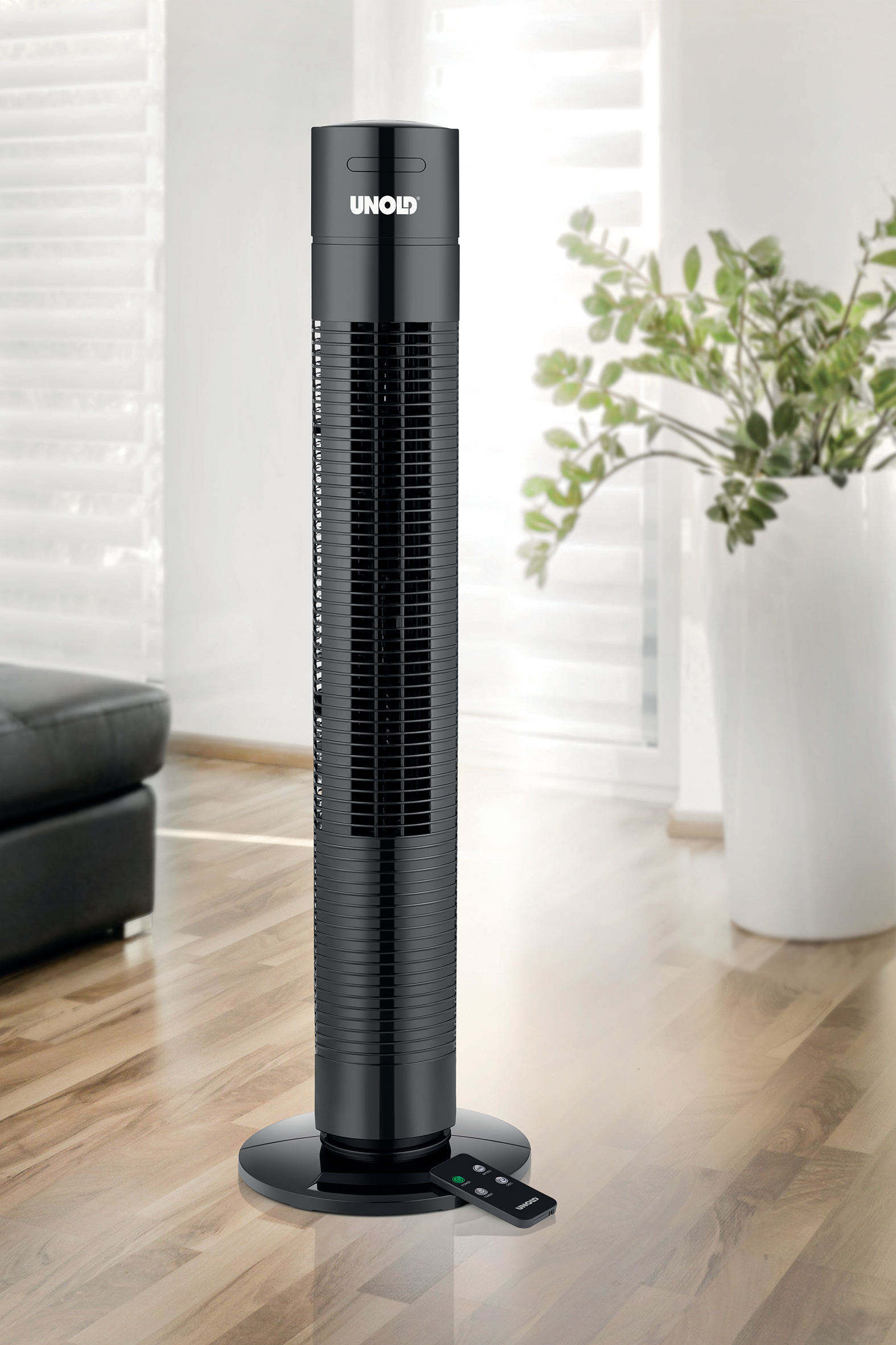 Schwarzer Unold Turmventilator auf Holzfußboden, Fernbedienung davor, weiße Vase mit Pflanze im Hintergrund.
