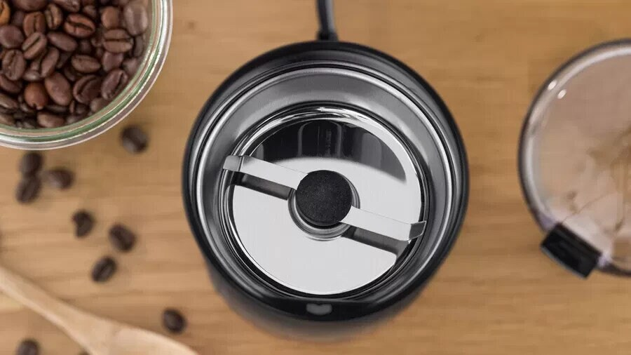 Widok z góry na młynek do kawy z ziarnami i filiżanką, na drewnianej powierzchni.