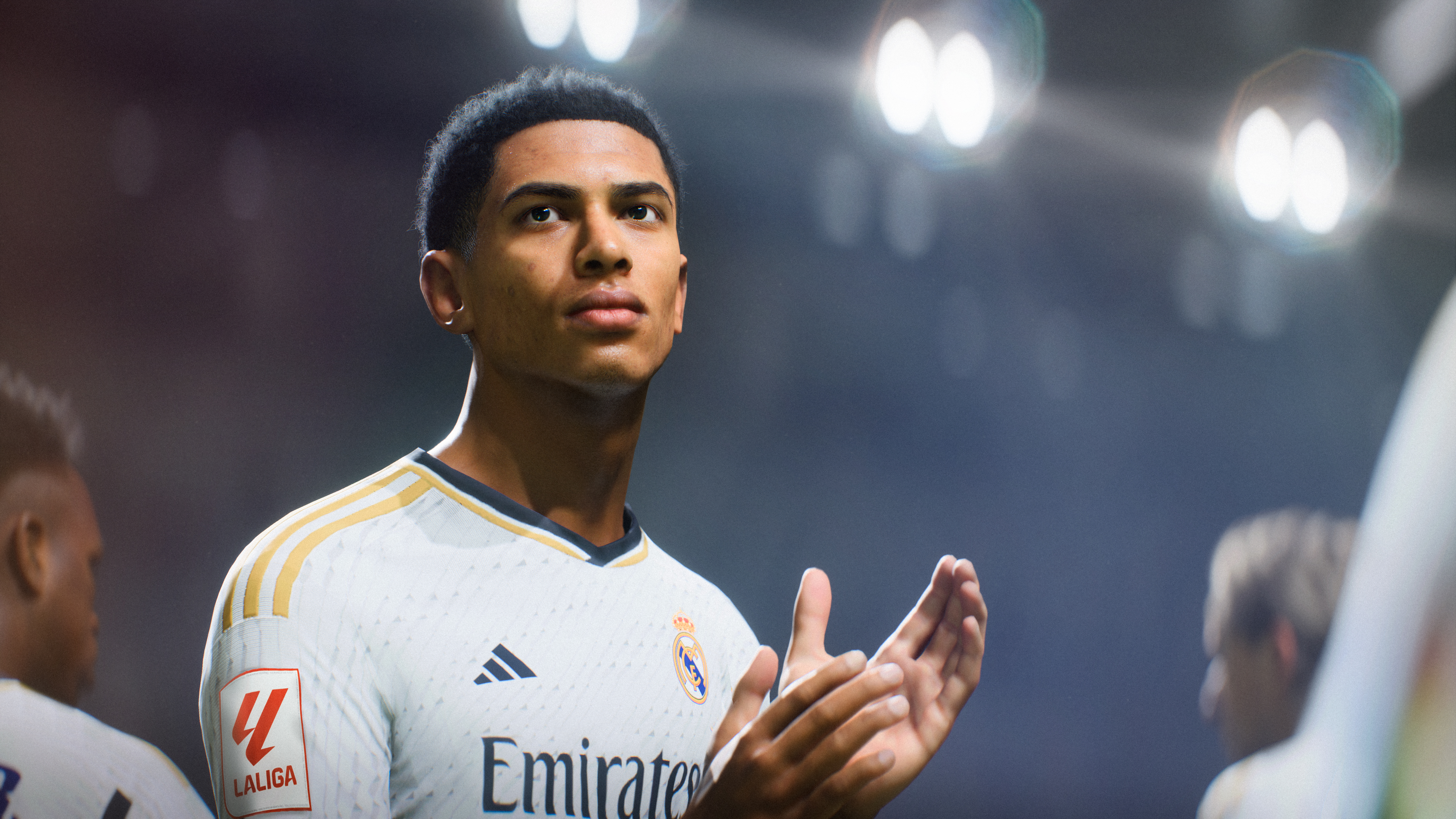 Een voetballer in een wit Real Madrid-shirt applaudisseert, met een stadion op de achtergrond.