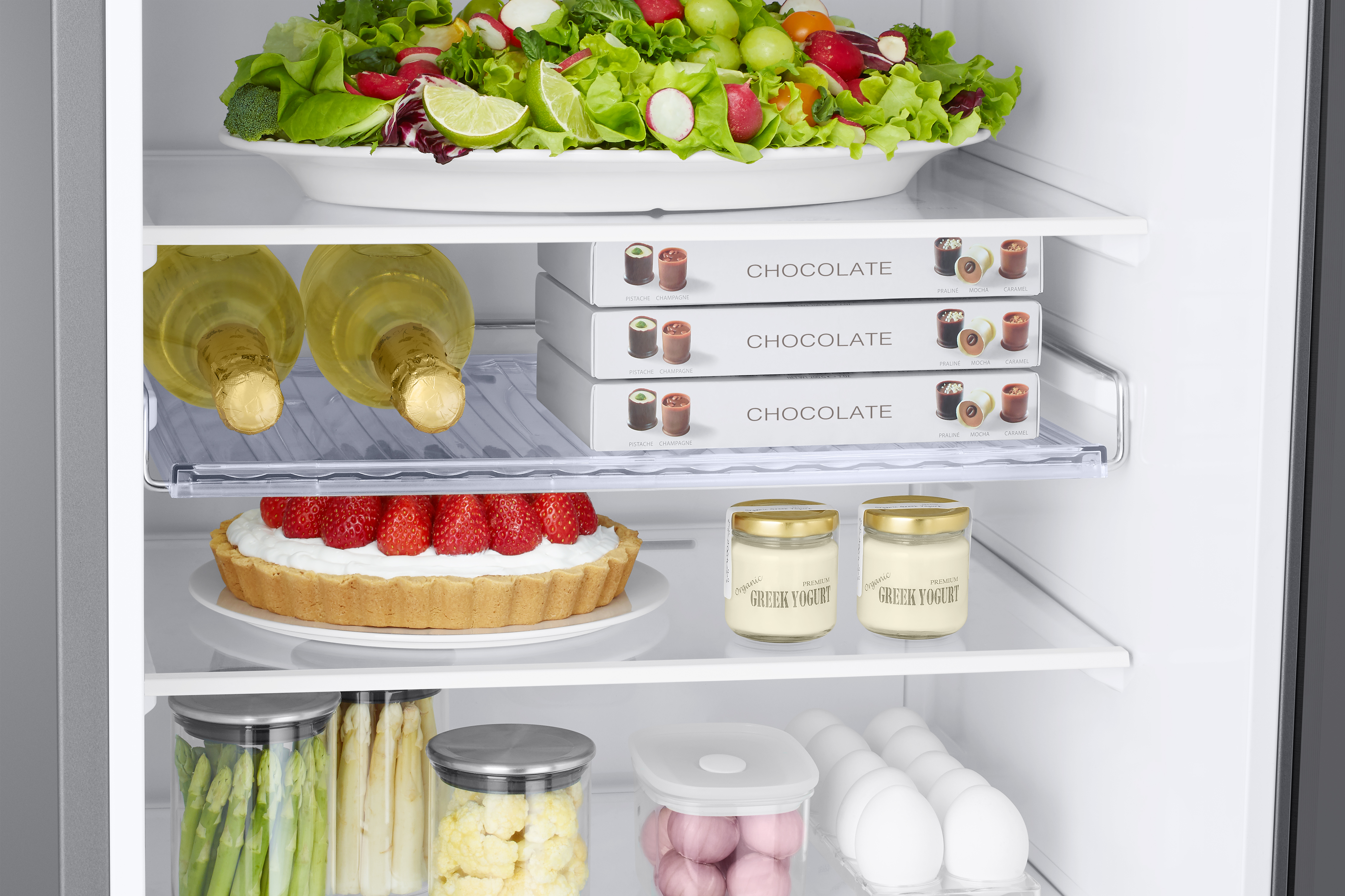 Kühlschrankinnenraum mit Salat, Schokolade, Weinflaschen, Joghurt und Obstkuchen.