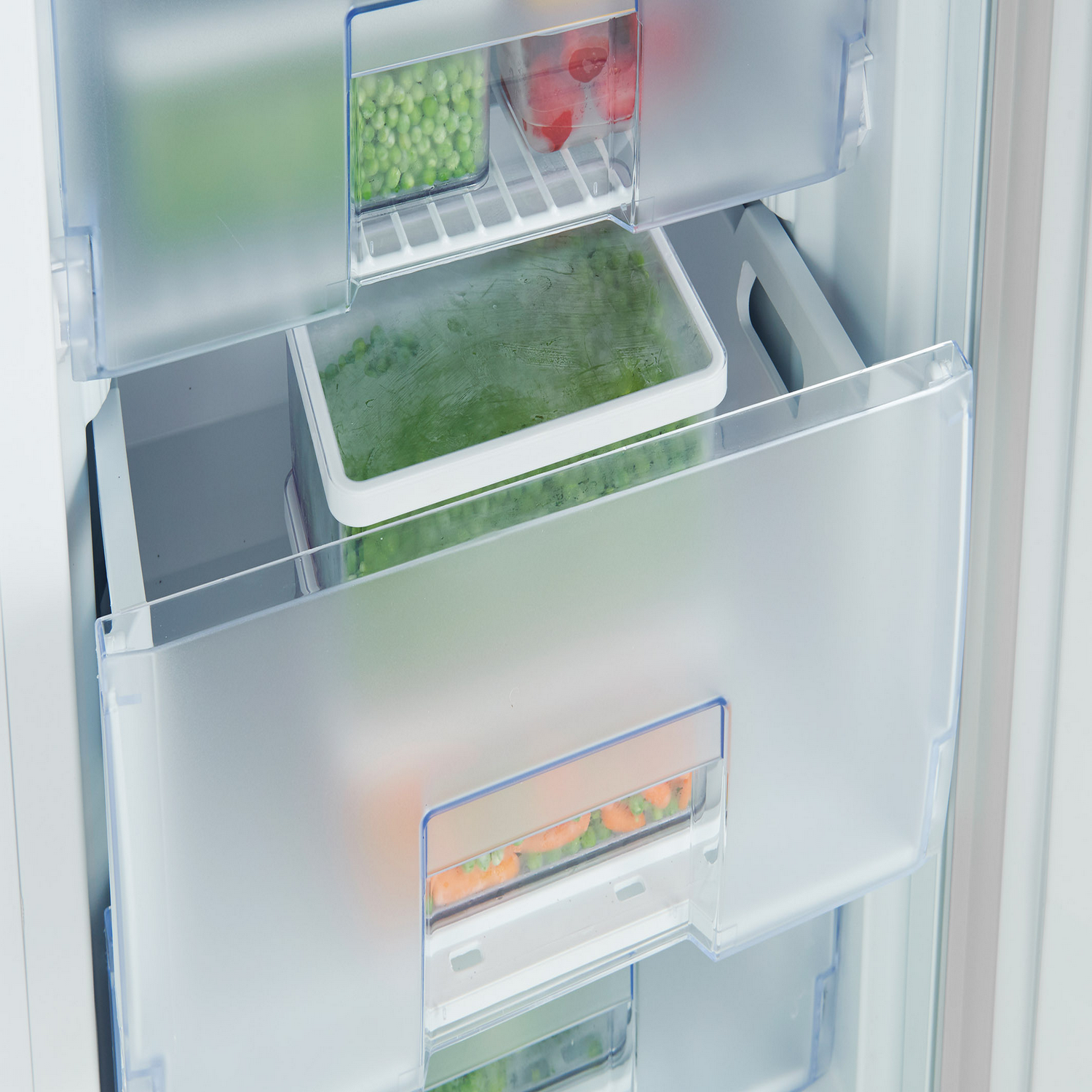 Open freezer drawers with vegetables in containers, close-up shot.