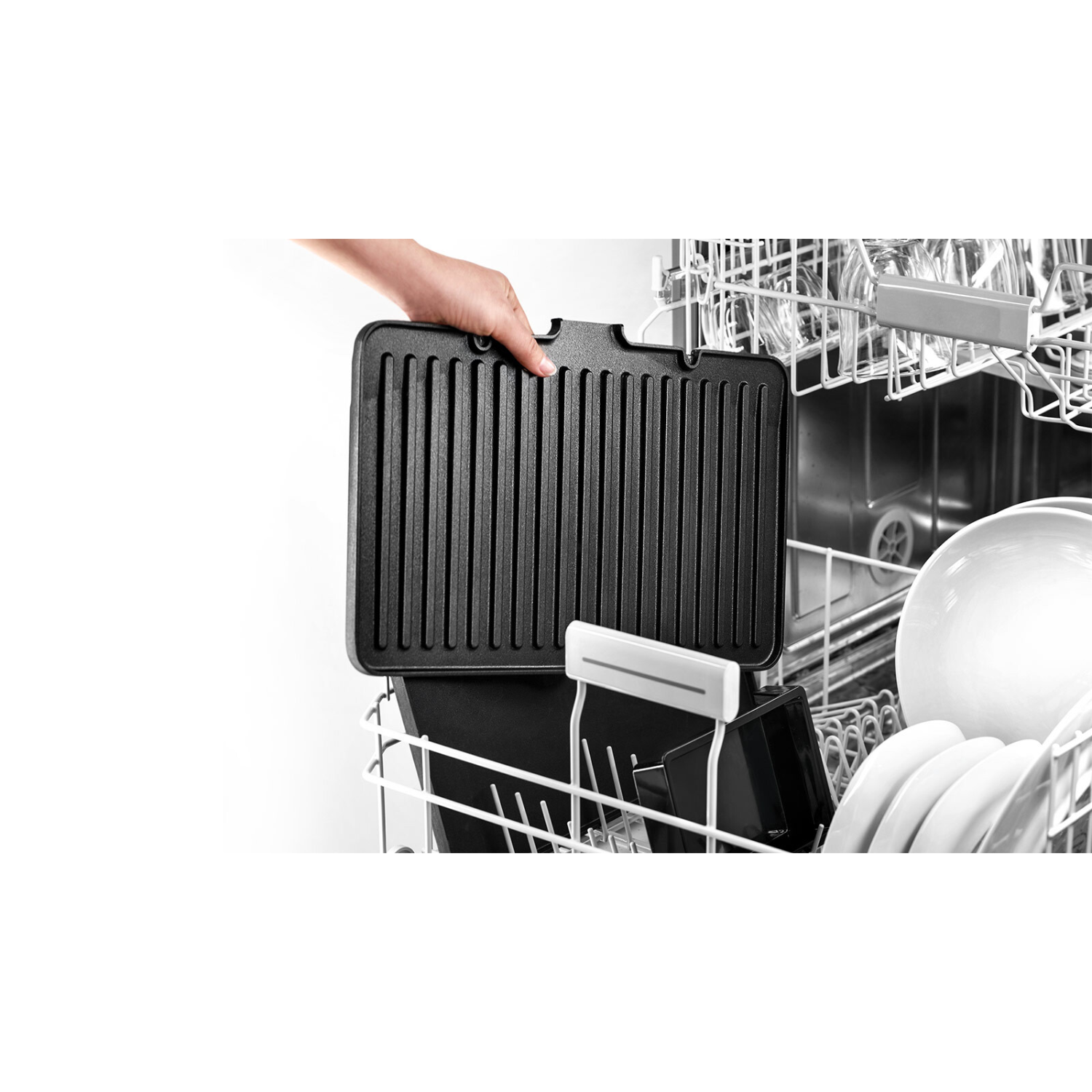 Een hand plaatst een zwarte grillplaat in een vaatwasser. Andere items en de vaatwasser zijn zichtbaar.