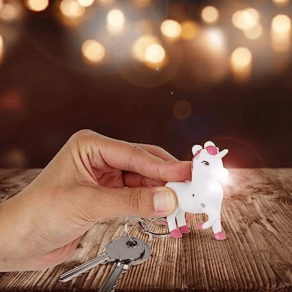 Una mano sostiene un llavero de unicornio blanco con detalles rosas y una luz. Llaves en primer plano.